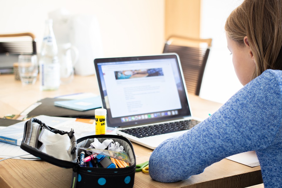 Student sits at a table and is engaged in remote learning activities via her laptop